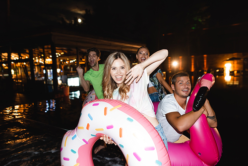 Selective focus of woman  near friends with swim rings during party at night