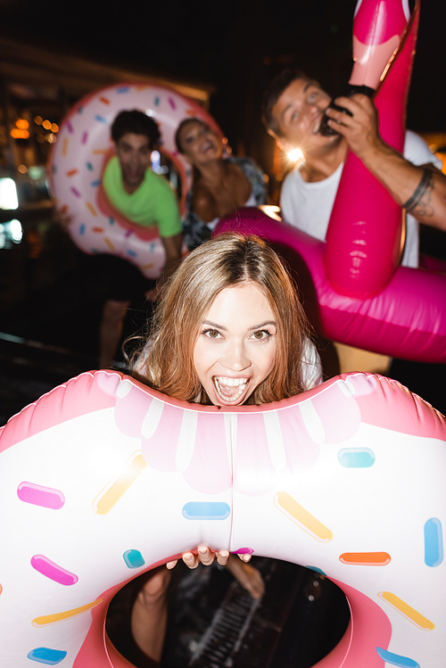 Selective focus of excited woman with swim ring  near friends at night