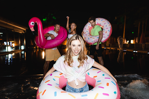 Selective focus of woman with swim ring  near friends and swimming pool at night