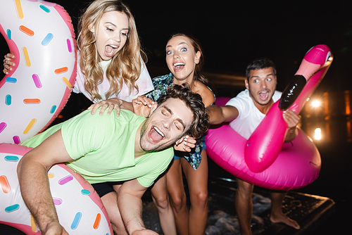 Selective focus of excited friends with swim rings standing near pool at night