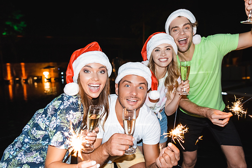 Selective focus of young people celebrating new year with champagne and sparklers at night outdoors