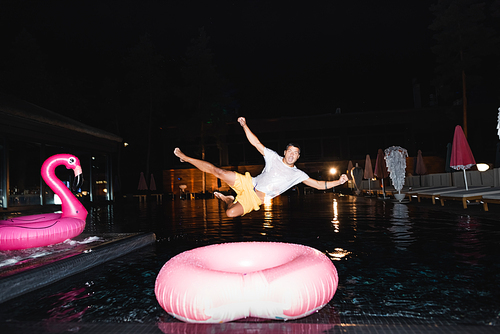 Selective focus of young man  while jumping in swimming pool at night