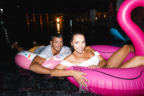 Selective focus of young couple  while swimming on rings in pool at night