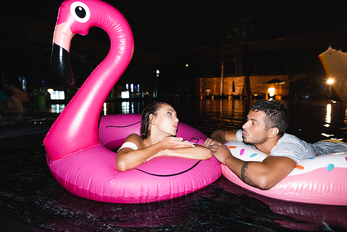 Young woman  to boyfriend while swimming in ring in pool at night