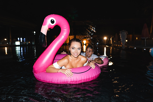 Selective focus of young woman  while swimming in ring near boyfriend in pool at night