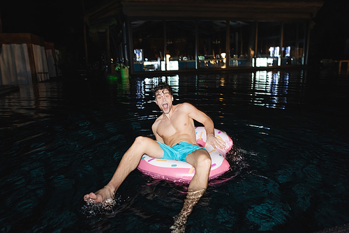 Selective focus of excited man sitting on swim ring in pool at night