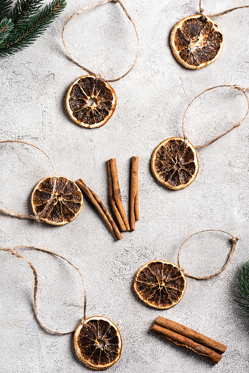 Top view of dried orange pieces with strings, cinnamon sticks and pine branches
