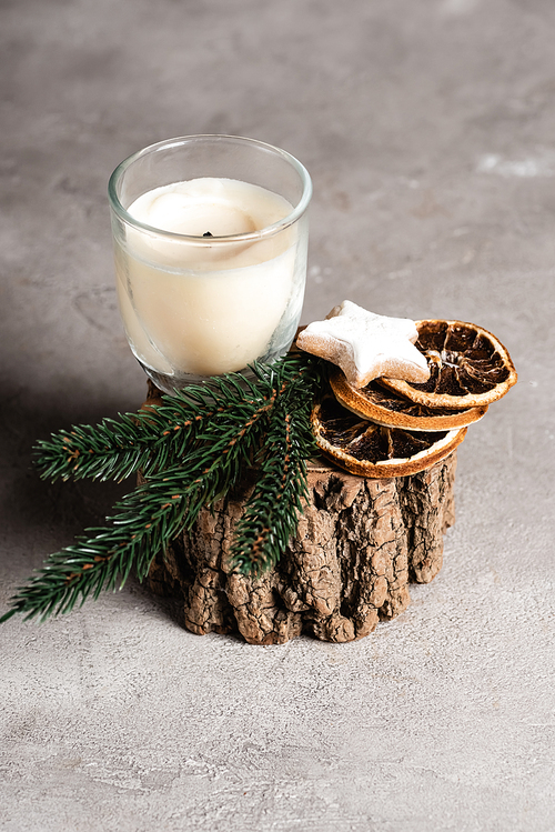 Scented candle with pine brunch, dried orange slices and cookie on wooden stand