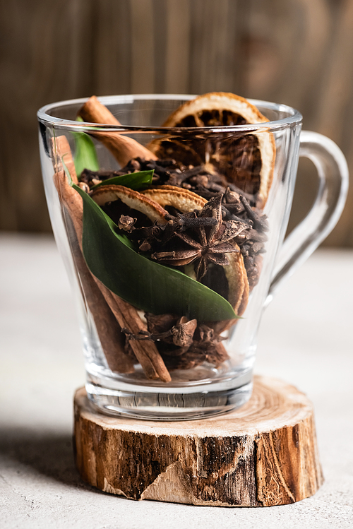 Selective focus of glass cup with spices and orange dried slices on wooden stand