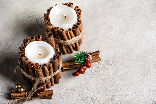 Scented candles decorated with cinnamon sticks on grey and textured background