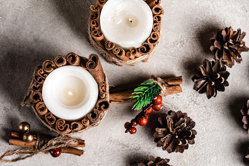 Top view of decorated candles with cinnamon sticks near pine cones and rowan