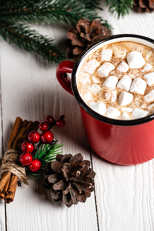 Cup of cocoa with marshmallows near cinnamon sticks with red beads and pine cone