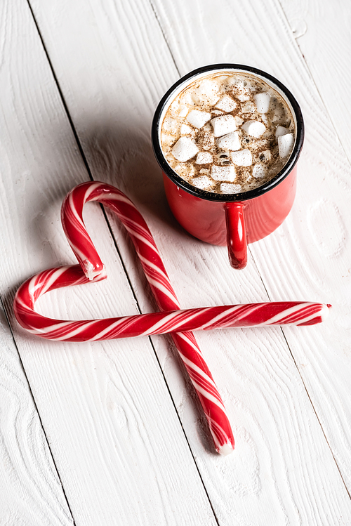 Red cup of cocoa near christmas candy canes in shape of love symbol