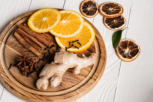 Wooden plate with spices, ginger root and orange slices on wooden background