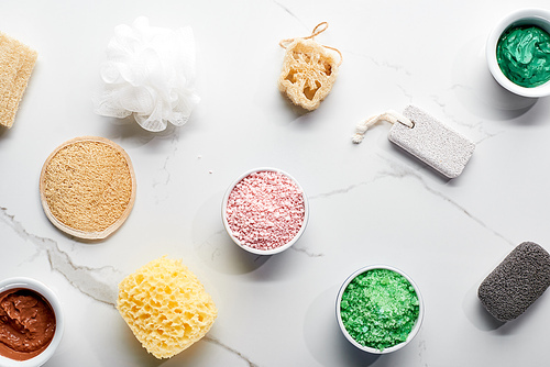 top view of color bath sponges, pumice stones, bath salts and clay mask on marble surface