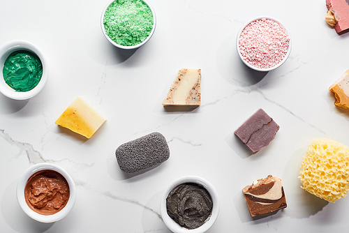 top view of bowls with bath salts, cosmetic mask, pieces of natural soap, pumice stone and bath sponge on marble surface