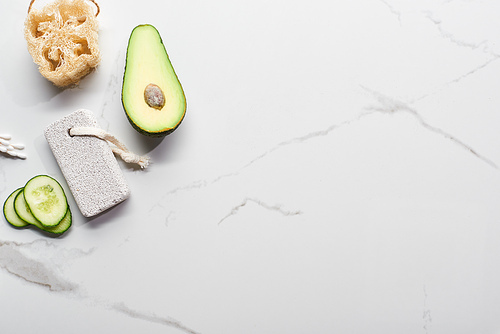 top view of fresh avocado and cucumber near loofah, ear sticks and pumice stone on marble surface