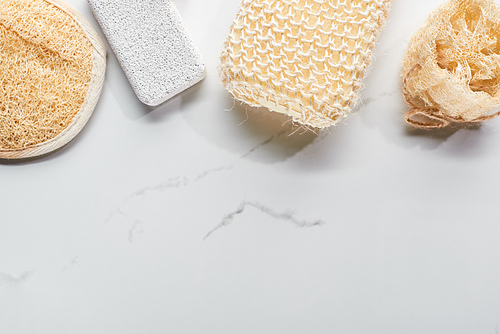 top view of pumice stone, loofah and bath sponges on marble surface