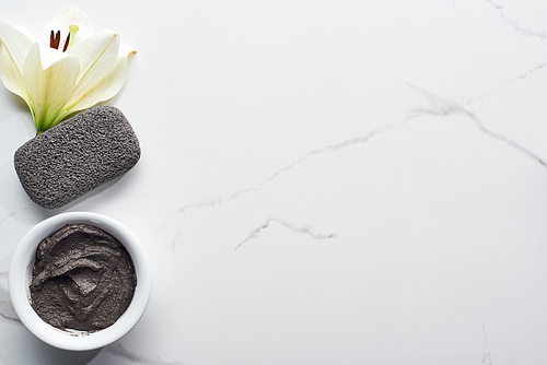 top view of natural clay mask and pumice stone near fresh flower on marble surface