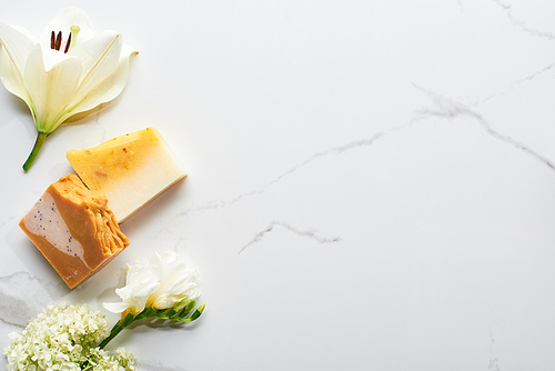 top view of natural soap pieces near fresh flowers on marble surface