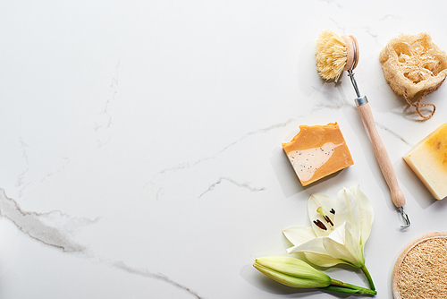 top view of natural soap pieces, body brush and loofah near fresh flower on marble surface