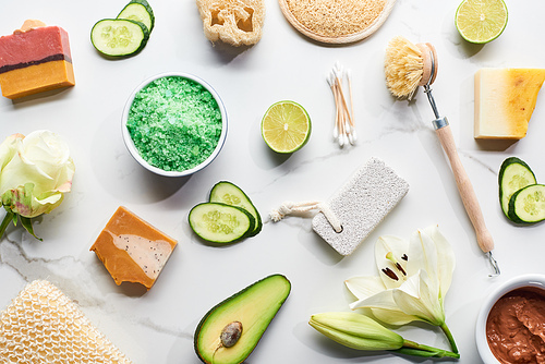 top view of natural beauty products and gadgets and soap pieces near fresh flowers, vegetables and fruit on marble surface