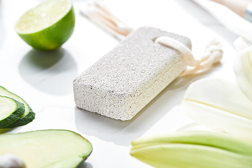 close up view of gray pumice stone near fresh lime and cucumber on white surface