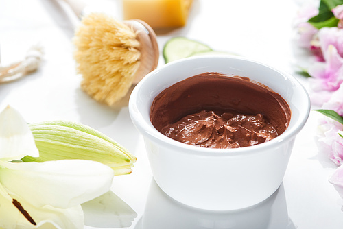 close up view of natural clay mask near body brush and flowers on white surface