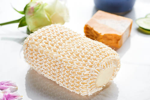 close up view of bath sponge near natural soap and flower on white surface