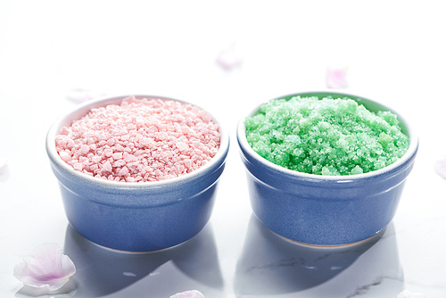 close up view of blue cups with bath salts on white surface with pink petals