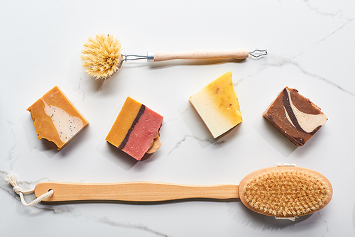 top view of homemade soap pieces and body brushes on marble surface