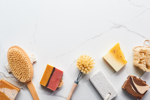 top view of homemade soap pieces, pumice stone and body brushes on marble surface