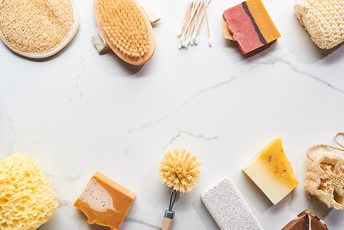 top view of homemade soap, pumice stone, bath sponges, ear sticks and body brushes on marble surface