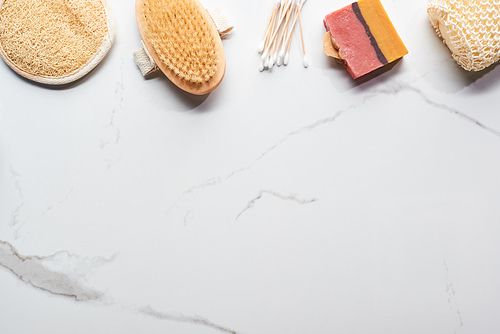 top view of homemade soap, bath sponges, ear sticks and body brush on marble surface