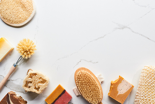 top view of homemade natural soap, loofah, bath sponges and body brushes on marble surface with copy space