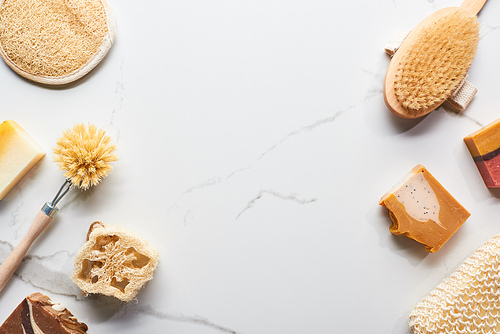 top view of loofah, bath sponges, body brushes and soap pieces on marble surface with copy space