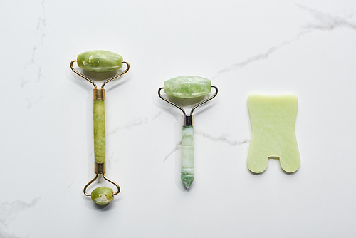 top view of jadeite facial rollers and spatula on marble surface