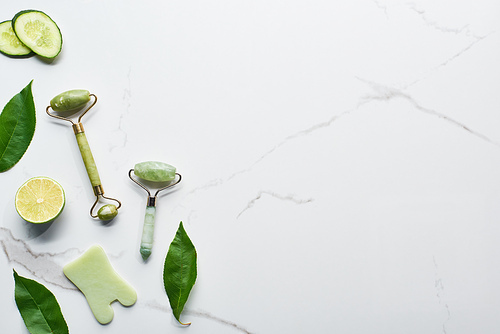 top view of spatula, massage rollers, fresh green leaves, lime and cucumber slices  on marble surface