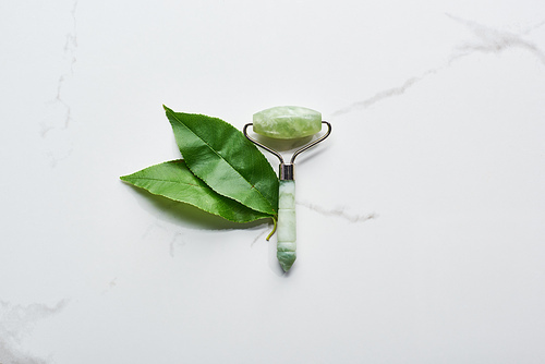 top view of jadeite facial roller and leaves on marble surface