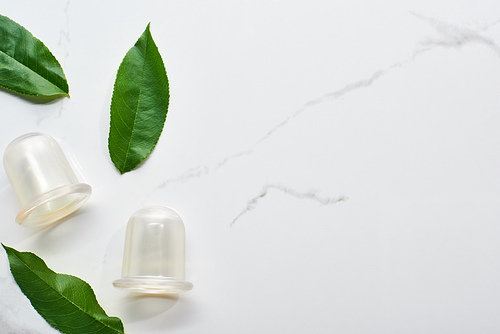 top view of massage vacuum jars and green leaves on marble surface