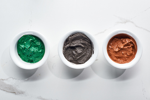 top view of cups with diverse natural face mask on marble surface