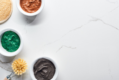 top view of brown, green and gray face mask near body brush and face sponge on marble surface