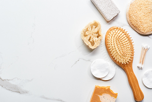 top view of cotton pads, ear sticks, loofah, pumice stone, face sponge and hair brush on marble surface