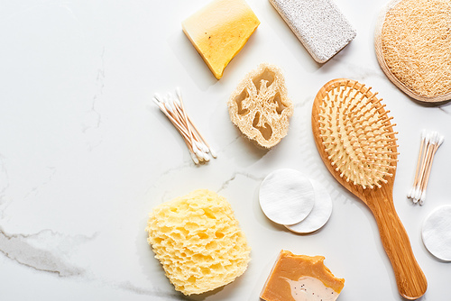 top view of hair brush, cotton swabs and pads, pumice stone and bath sponge on marble surface