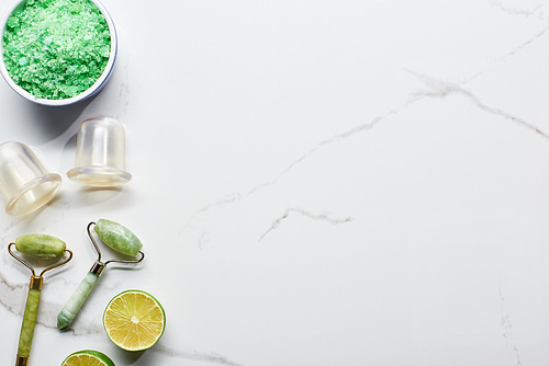 top view of massage jars and rollers near bath salts and lime on marble surface