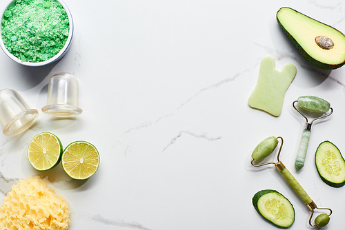 top view of massage jars, facial rollers, bath sponge and fresh fruits and vegetable on marble surface with copy space