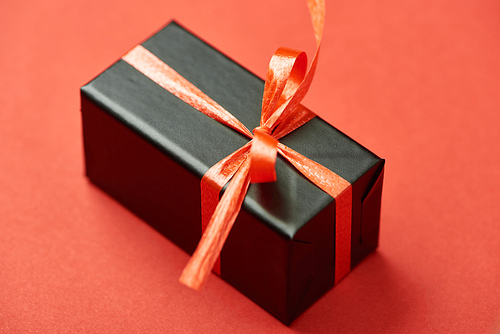 black gift box with bow and ribbon on red background