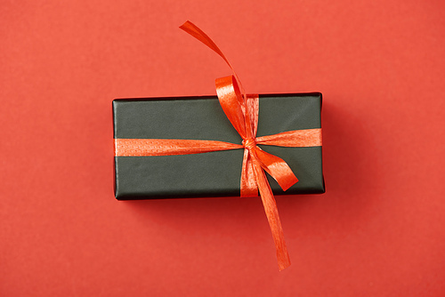 top view of black gift box with bow and ribbon on red background