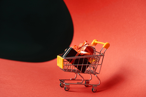 decorative gifts in small shopping cart on red paper isolated on black