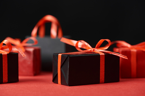 selective focus of presents with red ribbons and shopping bag isolated on black